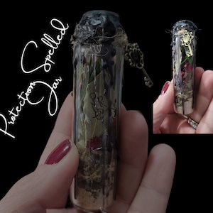 May include: A small glass jar filled with herbs, flowers, and other ingredients, sealed with black wax and a key charm. The jar is labeled "Protection Jar Spelled".