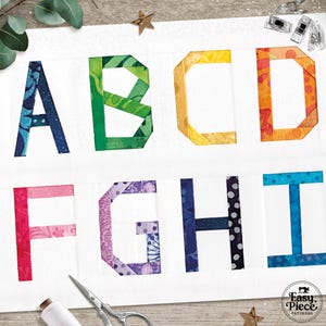 Puede incluir: Un panel de tela blanca con las letras A a la I, cada una hecha de piezas de tela coloridas y estampadas. Las letras están dispuestas en dos filas, con A, B, C y D en la fila superior y F, G, H e I en la inferior. Se ven accesorios de costura.