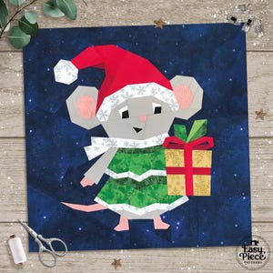 Op de afbeelding: Een stoffen kerstmuis met een rode kerstmuts en groene jurk, die een ingepakt cadeau vasthoudt. De muis staat tegen een donkerblauwe sterrenachtergrond. De afbeelding is een quiltblok met de tekst "Easy Piece Patterns".