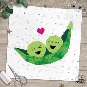May include: A fabric block featuring two smiling green peas in a pod with a pink heart above them. The background is white with a leaf pattern. The block is part of a quilting project.
