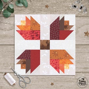 May include: A square quilt block with a geometric design in shades of red, orange, and brown. The block features a central square and four stylized leaf shapes. A spool of thread, scissors, and other sewing notions are visible.