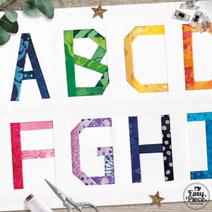 Puede incluir: Primer plano de una tela blanca con las letras A a la J, cada letra está hecha de tela de retazos colorida. Las letras están en un estilo de bloque en negrita. Herramientas de costura y estrellas decorativas están esparcidas alrededor de las letras.