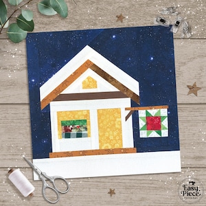 Puede incluir: Un bloque de edredón de tela que representa una casa con techo blanco, paredes amarillas y marco de puerta marrón. La casa tiene una ventana con un estampado de cuadros verdes y rojos. Un pequeño letrero con una estrella roja cuelga a un lado. El fondo es azul oscuro con estrellas blancas.
