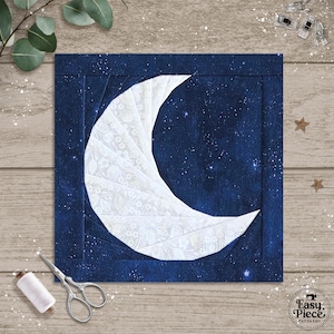 Könnte beinhalten: Ein quadratisches Stoffstück mit einem weißen Halbmond-Design auf einem dunkelblauen Sternenhimmel-Hintergrund. Der Mond besteht aus gemustertem Stoff. Das Stück hat einen dunkelblauen Rand. Nähwerkzeuge sind sichtbar.