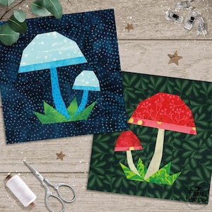 Può includere: Due quadrati di tessuto con disegni di funghi. Uno presenta un fungo blu su uno sfondo blu scuro a pois, l'altro un fungo rosso su uno sfondo verde a foglie. Attrezzi da cucito, forbici e filo sono sparsi.