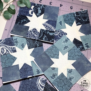 May include: Four square quilt blocks with a white star design in the center. The blocks are made of various blue patterned fabrics. The blocks are arranged on a purple cutting mat with a sprig of eucalyptus.