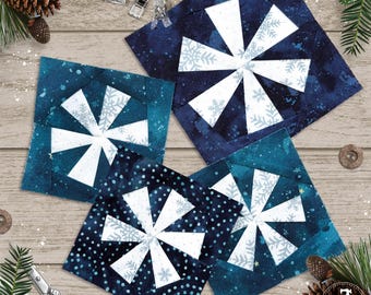 May include: Four square fabric quilt blocks featuring a pinwheel design with white snowflake patterns on dark blue and teal backgrounds. The blocks are arranged in a cluster, showcasing various shades of blue with white snowflake motifs.