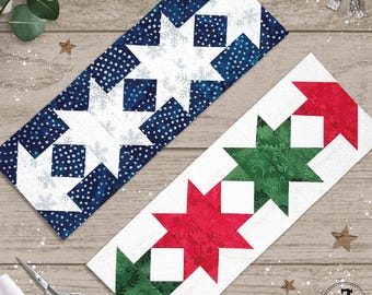 May include: Two rectangular quilt blocks featuring star patterns. One block has navy blue fabric with white dots and snowflakes paired with white stars. The other block features alternating red and green fabric stars with floral patterns on white.