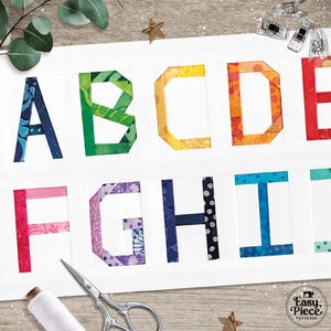 Puede incluir: Primer plano de una tela blanca con las letras A a la I, cada letra es de un color y patrón diferente. Las letras están hechas de trozos de tela cosidos. Se ven suministros de costura, incluyendo tijeras e hilo.