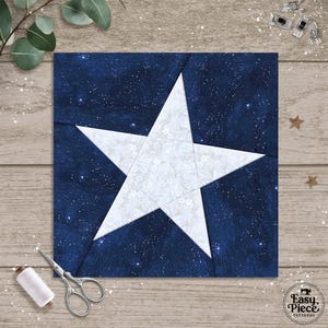 May include: A square fabric piece featuring a large white star against a dark blue, starry background. The star is composed of smaller white floral patterns. Sewing tools, including scissors and thread, are visible, suggesting a quilting or crafting theme.
