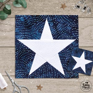 May include: A large, square fabric block with a white star design against a dark blue background with white polka dots. A smaller version of the block is next to it. Sewing tools and a spool of thread are also visible.