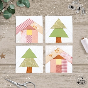 May include: Four square fabric blocks with house and tree designs. The houses have pink, yellow, and white patterned roofs and walls. The trees are green with orange trunks. The blocks are on a light wood surface.
