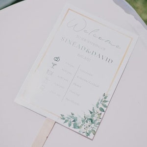 Puede incluir: Un programa de ceremonia de boda blanco con un diseño floral y el texto "Bienvenido a la boda de Sinead & David 11.07.2022" impreso en él.