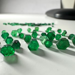 Puede incluir: Una colección de pequeñas piedras preciosas verdes facetadas dispuestas en línea sobre una superficie blanca.