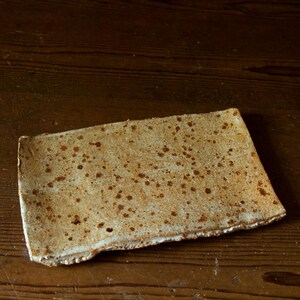May include: A rectangular ceramic plate with a speckled, textured surface. The plate has a light brown colour with darker brown spots and a white edge. The handmade pottery has a rustic, organic aesthetic.