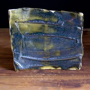 May include: A ceramic tile with a textured surface and a blue-green glaze. The glaze has a mottled appearance with streaks of yellow and brown.
