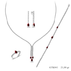 May include: A jewelry set consisting of a necklace, a bracelet, a ring, and a pair of drop earrings. Each piece is crafted from silver-toned metal and features clear round stones and pear-shaped red stones. The set is labeled GTK041 21.00 gr.