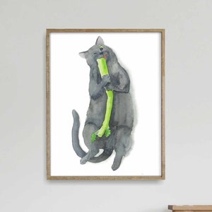 May include: A watercolor painting of a gray cat eating a green stalk of celery. The cat is sitting up on its hind legs and holding the celery in its paws. The painting is framed in a light brown frame.