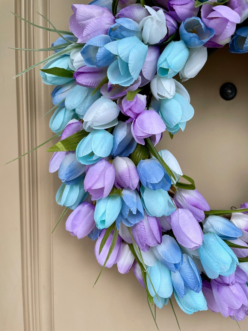 May include: A wreath made of artificial blue and purple tulips. The wreath is made of a variety of shades of blue and purple, and the tulips are arranged in a circular pattern.