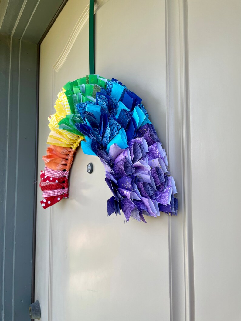 May include: A rainbow-colored fabric wreath with a red and white checkered bow hanging on a white door.