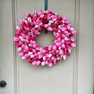 May include: A pink and white tulip wreath hanging on a white door. The wreath is made of artificial tulips and is a great way to add a touch of spring to your home.
