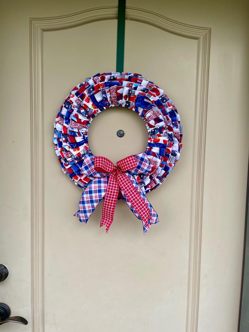 May include: A red, white, and blue fabric wreath with a red and white plaid bow. The wreath is made of fabric scraps and is decorated with stars and stripes.