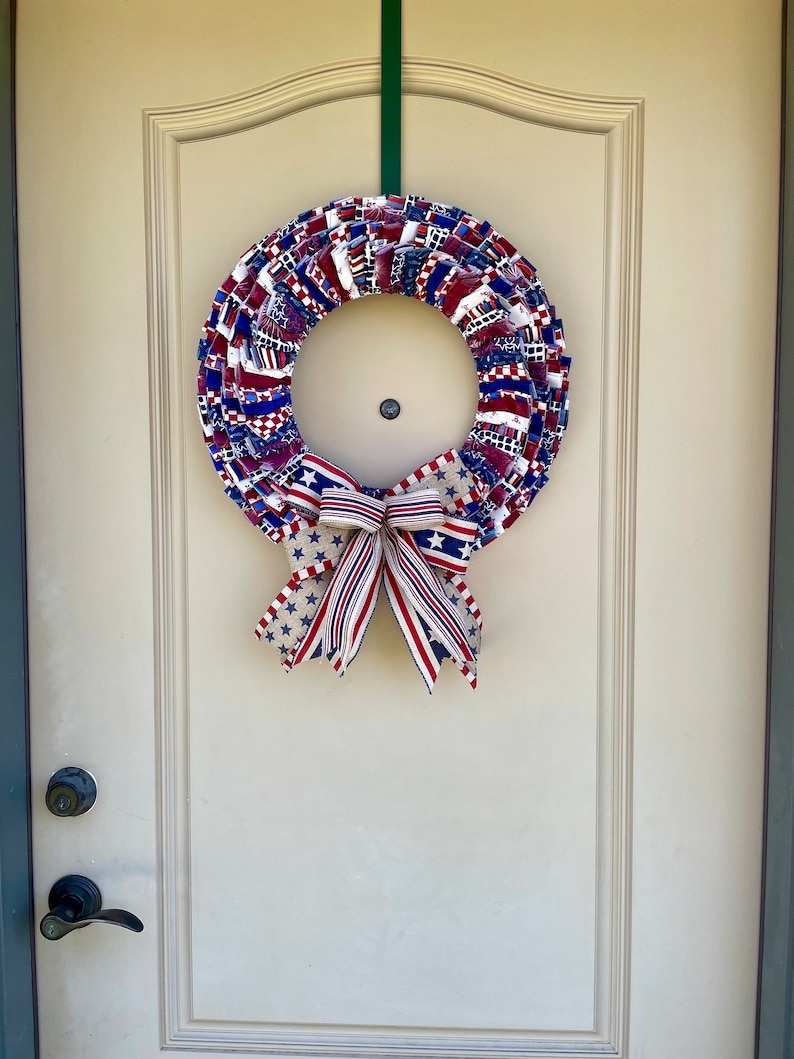 May include: A red, white, and blue fabric wreath with a star-patterned bow. The wreath is hanging on a white door.