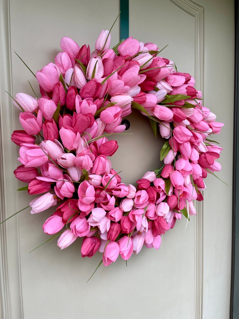 May include: A pink and white tulip wreath with green stems. The wreath is made of artificial flowers and is ideal for spring decor.
