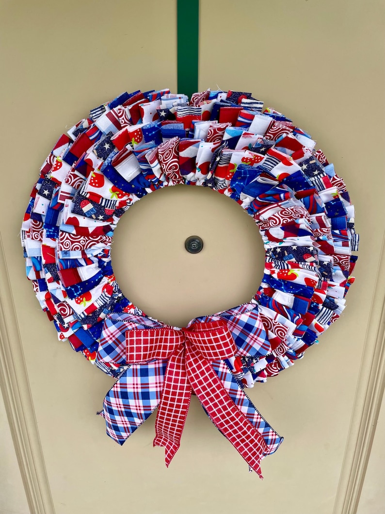 May include: A red, white, and blue fabric wreath with a plaid bow. The wreath is made of various patriotic fabrics with stars, stripes, and strawberries.