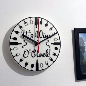 Könnte beinhalten: Eine weiße, runde Wanduhr mit schwarzen Zeigern und dem Text "It's Wine O'Clock!". Das Zifferblatt zeigt schwarze Weingläser und -flaschen am Rand. Der Sekundenzeiger ist rot.
