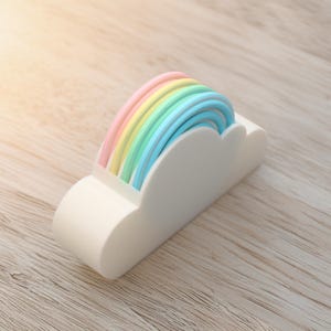 May include: A white cloud-shaped desk tidy with a rainbow design. The rainbow features pastel shades of pink, yellow, green, and blue. The organiser is made of a solid material and sits on a wooden surface.