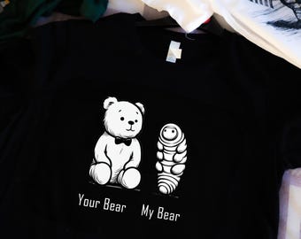 Puede incluir: Camiseta negra con un gráfico blanco de un oso de peluche con pajarita y un gusano. El texto "Your Bear" y "My Bear" está impreso debajo del gráfico.