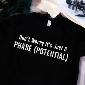 May include: Black t-shirt with white text that reads "Don't Worry It's Just A PHASE (POTENTIAL)"