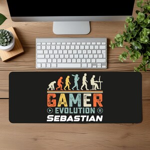 Könnte beinhalten: Schwarze Gaming-Mausmatte mit einer Retro-Illustration der Evolution eines Gamers, vom Höhlenmenschen bis zu einer Person, die ein Videospiel spielt. Der Text "GAMER EVOLUTION" ist in einer bunten Schriftart geschrieben, und der Name "SEBASTIAN" steht darunter.