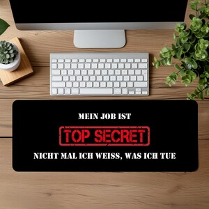 Könnte beinhalten: Schwarze und rote Mauspad mit dem Text "Mein Job ist Top Secret Nicht mal ich weiss, was ich tue" in weiß.