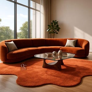 May include: A contemporary living room arrangement with a large, curved terracotta sofa, an armchair, and a distinctive rug. A glass coffee table and cushions add to the inviting atmosphere. The room is filled with natural light.
