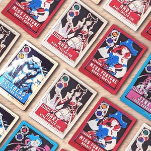 Puede incluir: Una colección de tarjetas rectangulares con ilustraciones de personajes y texto. Las tarjetas presentan personajes como Miss Fortune, Ahri y Volibear, con texto como "Bounty Hunter" y "Nine-Tailed Fox". Las tarjetas tienen bordes rojos, azules y blancos.