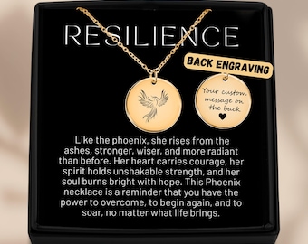 Könnte beinhalten: Goldfarbene Halskette mit rundem Anhänger mit Phönix-Design. Die Halskette wird in einer schwarzen Schachtel mit dem Wort "RESILIENCE" oben präsentiert. Der Anhänger hat eine zweite Seite für eine individuelle Gravur.