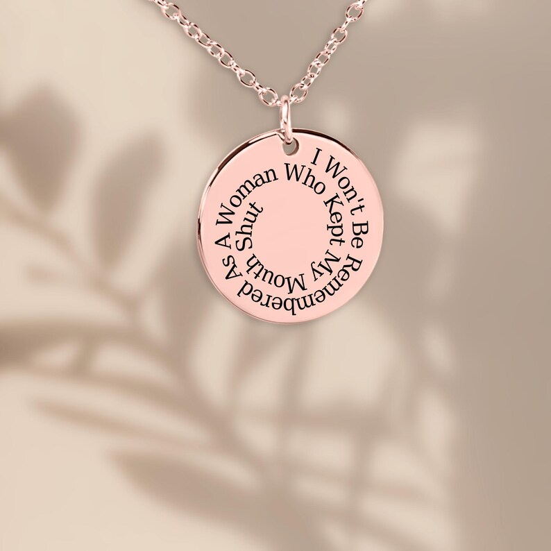 Puede incluir: Collar con colgante de color oro rosa. El colgante redondo presenta el texto grabado: "Como mujer, no ser&eacute; recordada por quien se call&oacute; la boca."