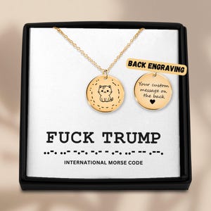 May include: A gold-colored necklace with two round pendants, one featuring a cat illustration and the other with the text "Your custom message on the back". The box reads "FUCK TRUMP" in bold letters and Morse code.