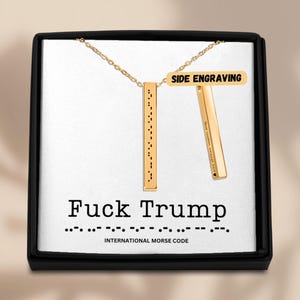 Peut inclure: Un collier doré avec un pendentif en forme de barre verticale avec du code Morse. Le collier est présenté dans un coffret noir avec le texte "Fuck Trump" et "Code Morse International". Une deuxième barre est incluse avec les mots "Side Engraving".