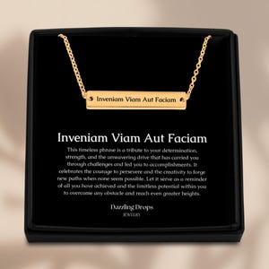 May include: A gold necklace with a bar pendant that reads "Inveniam Viam Aut Faciam". The necklace is in a black box with a white background and a message about the meaning of the phrase.