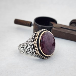 May include: A silver ring with an ornate design and a large, oval-shaped red gemstone set in a gold bezel.