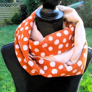 Könnte beinhalten: Ein orangefarbener Schal mit weißen Punkten. Der Schal ist um eine schwarze Schaufensterpuppe drapiert. Der Schal hat eine doppelte Schicht, mit dem orangefarbenen Stoff mit Punkten außen und einem cremefarbenen Stoff innen.