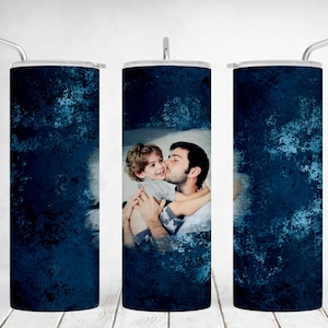 May include: A stainless steel tumbler with a blue and white distressed background. A photo of a father and son is centered on the tumbler. The father is kissing the son on the cheek.