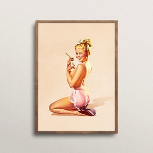 May include: A framed art print featuring a blonde person with an updo hairstyle, kneeling while wearing pink shorts with white lace trim. The person is winking and holding a small rectangular object with text in their hand.
