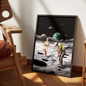 May include: A framed print of a surrealist artwork depicting a man and woman playing golf on the moon. The moon's surface is cratered, and Earth is visible in the background. The artwork is set against a black background with stars.