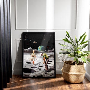 May include: A framed print of a surrealist artwork depicting a man and a woman playing golf on the moon. The moon is depicted with craters and a dark sky with stars. The artwork is in a black frame.