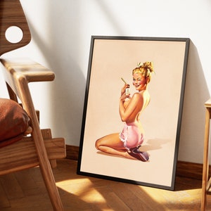 May include: A framed art print featuring a vintage-style illustration of a person with blonde hair kneeling while wearing pink ruffled shorts. The person is holding a small bottle with a label that reads 'SUN TAN LOTION' and is smiling.