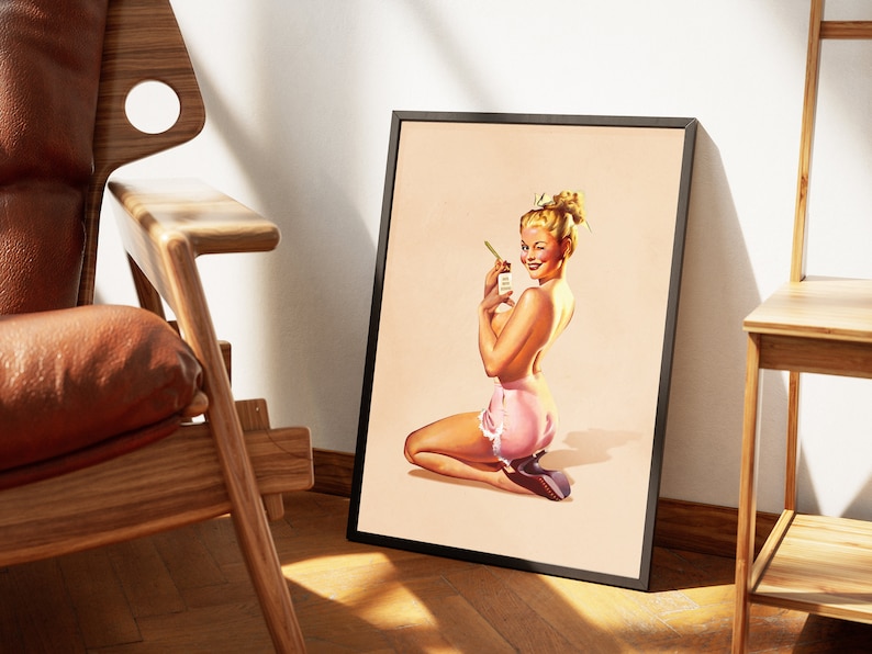 May include: A framed art print featuring a vintage-style illustration of a person with blonde hair kneeling while wearing pink ruffled shorts. The person is holding a small bottle with a label that reads 'SUN TAN LOTION' and is smiling.